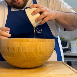 Un uomo con un grembiule che versa del liquido in una ciotola di legno