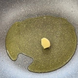 Un pezzo di aglio viene cotto in una padella con olio.