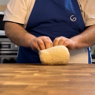 Un uomo con un grembiule blu sta impastando una palla di pasta