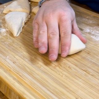 Una persona sta impastando l'impasto su un tagliere di legno.