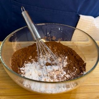 Una ciotola di vetro piena di cacao in polvere e zucchero con una frusta al suo interno