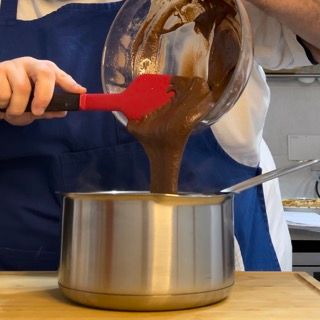 Una persona che versa il cioccolato in una pentola con una spatola rossa