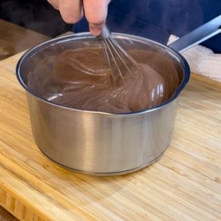 Una persona sta mescolando una pentola di salsa al cioccolato su un tagliere di legno.