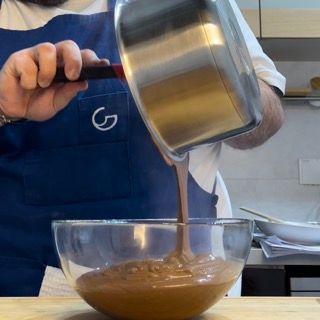 Un uomo con un grembiule blu che versa il cioccolato in una ciotola