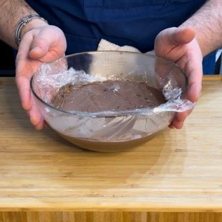 Una persona tiene in mano una ciotola ricoperta di pellicola trasparente