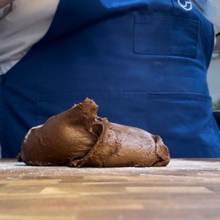 Una persona con un grembiule blu sta impastando la pasta su un tagliere