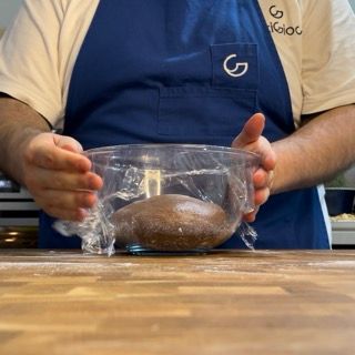 Un uomo con un grembiule blu tiene in mano una ciotola di pasta