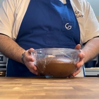 Un uomo con un grembiule blu tiene in mano una ciotola di cioccolato