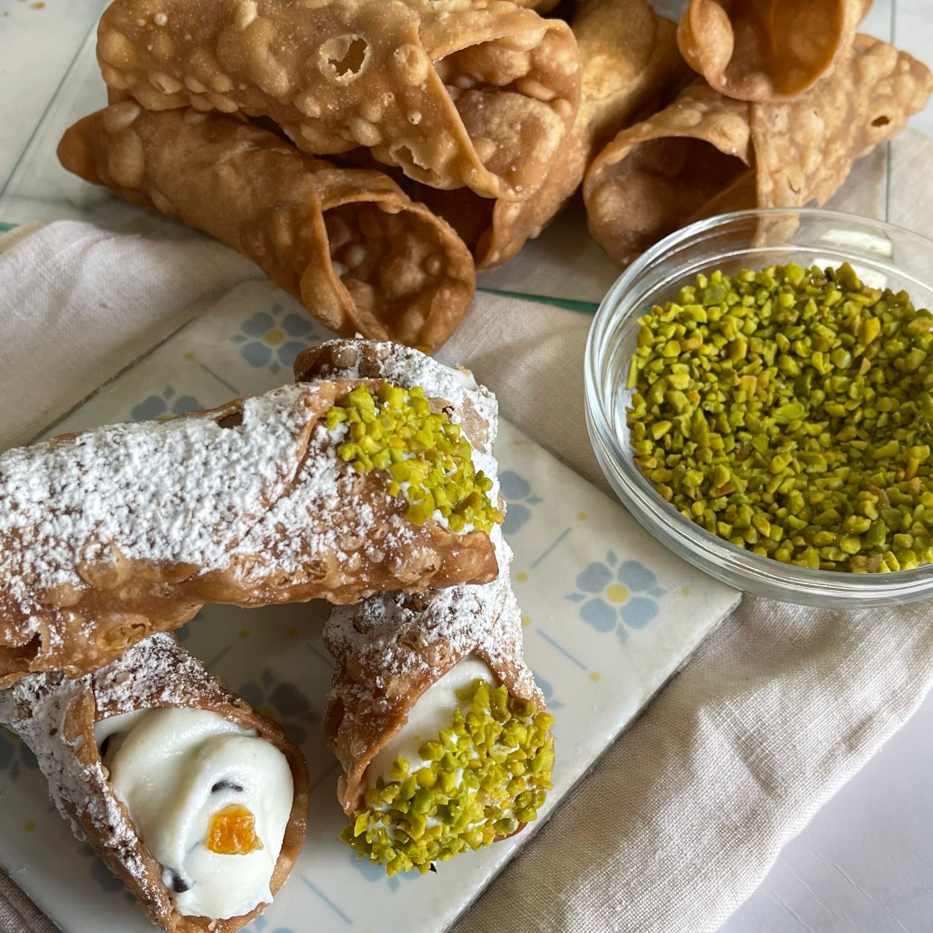 Un piatto di cannoli con zucchero a velo e pistacchi accanto a una ciotola di pistacchi