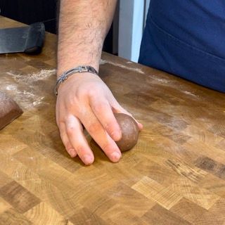 Una persona tiene in mano una palla di pasta su un tagliere di legno.