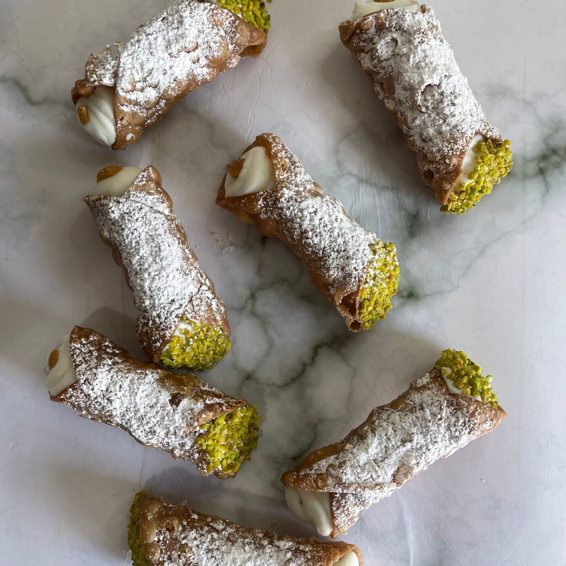 Un gruppo di cannoli con zucchero a velo e pistacchi su una superficie di marmo.