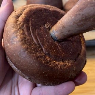 Una persona tiene in mano una ciambella al cioccolato con un bastoncino di legno che sporge da essa
