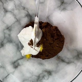 Una ciotola di cioccolato in polvere e panna montata con un cucchiaio dentro.