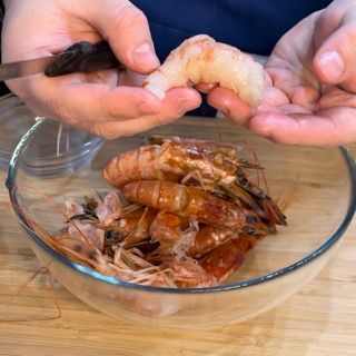 Una persona tiene in mano un gambero sopra una ciotola di gamberi