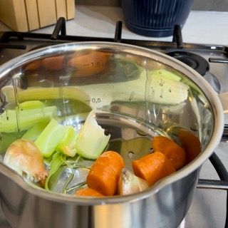 Una pentola piena di carote, sedano e cipolle è sul fornello.