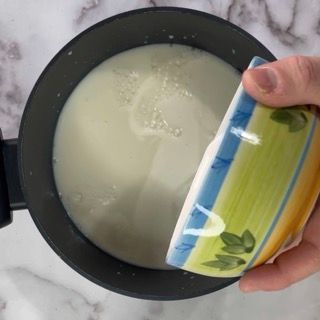 Una persona sta versando una ciotola di latte in una pentola.