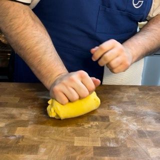 Un uomo con un grembiule sta impastando la pasta su un tagliere di legno