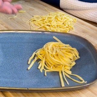 Un piatto blu con sopra delle tagliatelle su un tavolo di legno