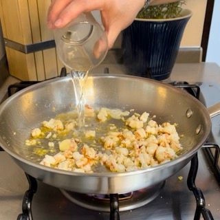 Una persona che versa acqua in una padella con gamberetti