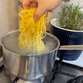 Una persona sta versando i noodles in una pentola d'acqua