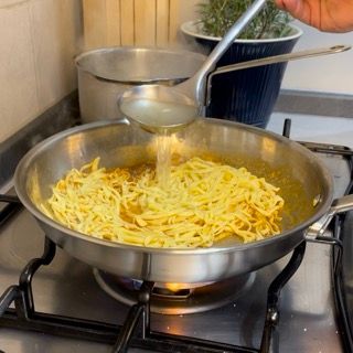 Una persona sta versando del liquido in una padella di tagliatelle