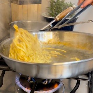 Una persona sta cucinando le tagliatelle in una padella sul fornello