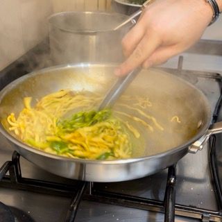 Una persona sta mescolando le tagliatelle in una padella sul fornello