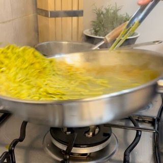 Una persona sta mescolando le tagliatelle in una padella sul fornello