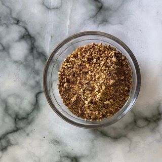 Una piccola ciotola di vetro piena di polvere marrone su una superficie di marmo