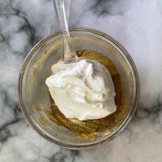 Una ciotola di vetro piena di panna montata e miele con un cucchiaio dentro.