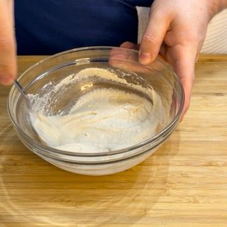 Una persona sta mescolando qualcosa in una ciotola di vetro su un tavolo di legno.