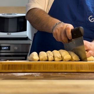 Un uomo con un grembiule blu sta tagliando la pasta su un tagliere di legno