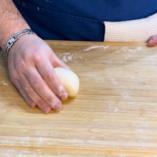 Una persona tiene in mano una palla di pasta su un tagliere di legno.