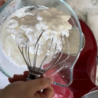 Una persona tiene una frusta sopra una ciotola di panna montata