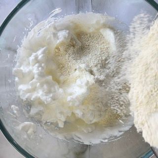 Una persona versa la farina in un frullatore pieno di panna montata.