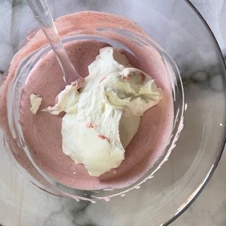 Una ciotola di frullato di fragole con panna montata e un cucchiaio dentro