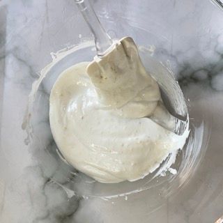 Un primo piano di una ciotola di besciamella con un cucchiaio dentro.