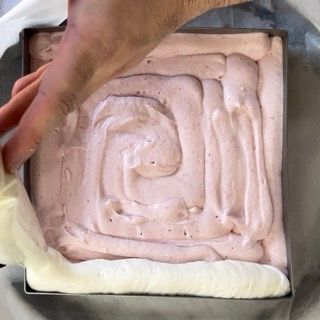 Una persona sta stendendo vortici di glassa rosa e bianca su una teglia quadrata