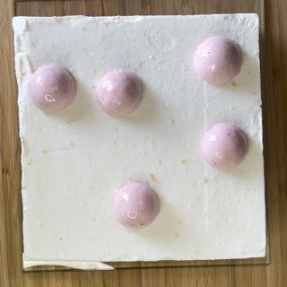 Una fetta di torta quadrata con delle palline rosa sopra su un tavolo di legno.