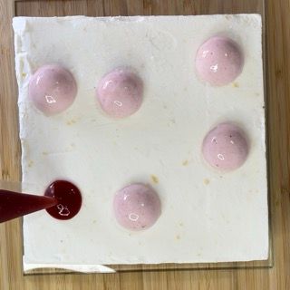 Un primo piano di una fetta di torta con palline rosa sopra su un tavolo di legno.