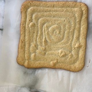 Un biscotto quadrato con una spirale sopra è appoggiato su un pezzo di carta oleata.