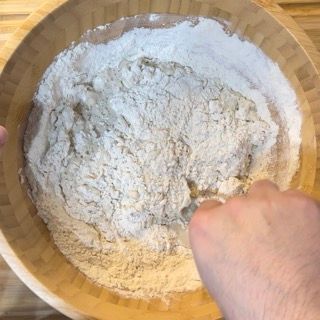 Una persona sta mescolando la farina in una ciotola di legno.