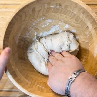 Una persona tiene in mano un pezzo di pasta in una ciotola di legno