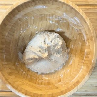 Una ciotola di legno piena di impasto è appoggiata su un tavolo di legno.