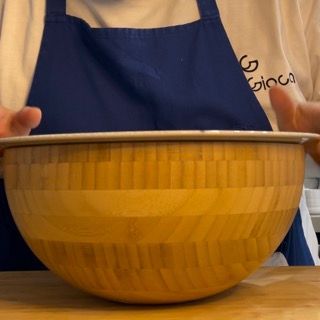 Una persona che indossa un grembiule blu tiene in mano una ciotola di legno