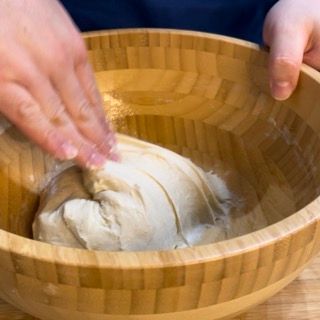 Una persona sta mescolando l'impasto in una ciotola di legno.