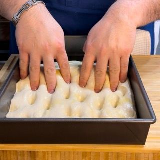 Una persona sta mettendo le mani su una teglia di pasta