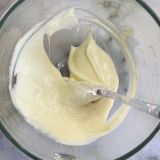 Una ciotola di vetro piena di glassa bianca e una spatola.