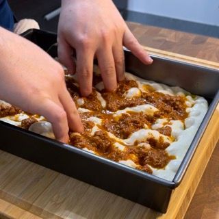 Una persona sta mettendo la salsa su una pizza in una padella