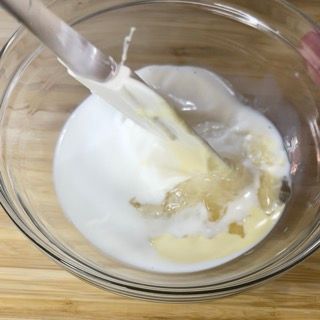 Una ciotola di liquido con un cucchiaio dentro su un tavolo di legno.